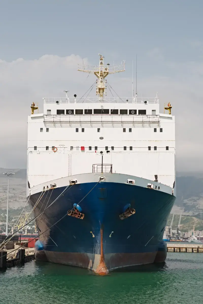 A ro-ro vessel moored bow-on alongside a commercial quay, mooring lines made fast, with port cranes behind